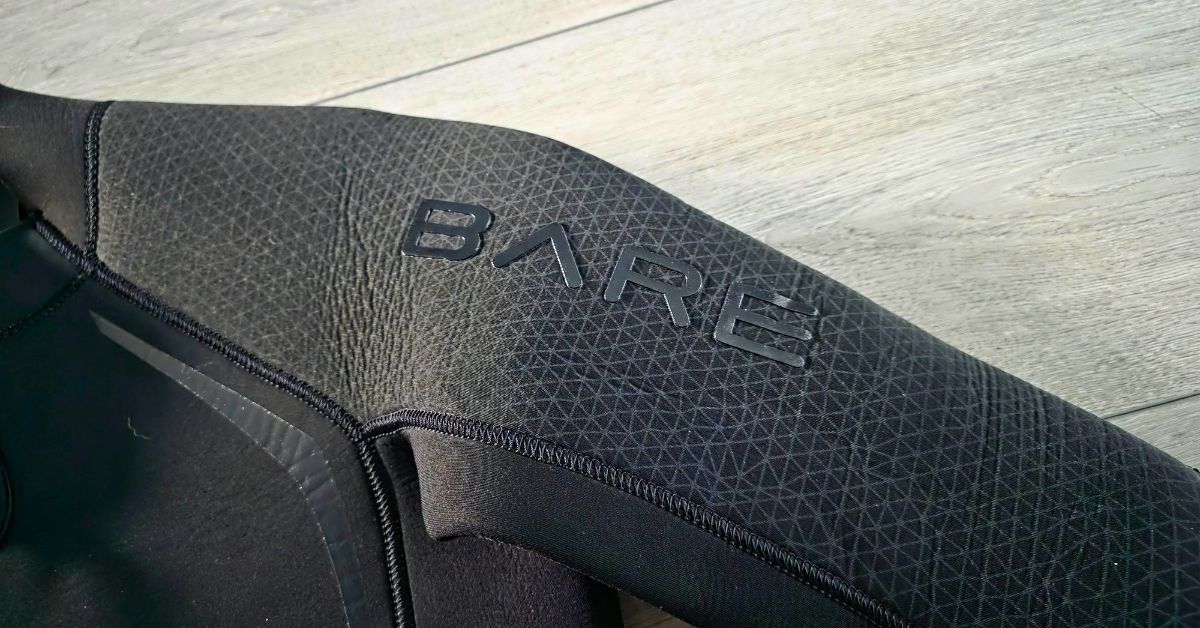 Close up of logo on shoulder of BARE Reactive 5mm wetsuit showing wear from dozens of uses. For article titled BARE Reactive 5mm Wetsuit Review.